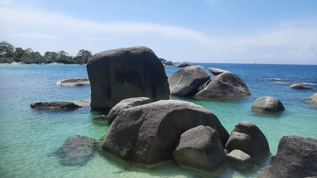 Batu granit besar di perairan dangkal biru kehijauan di Pantai Tanjung Tinggi, Kabupaten Belitung.